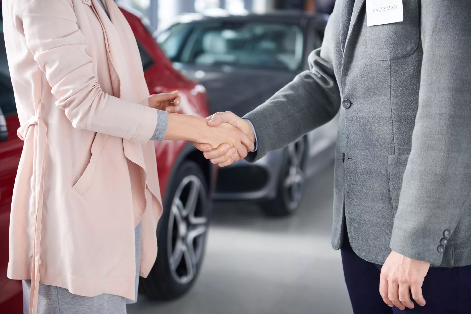 汽車展示間內，顧客與銷售人員在車輛旁握手，象徵完成購車或交易協議。