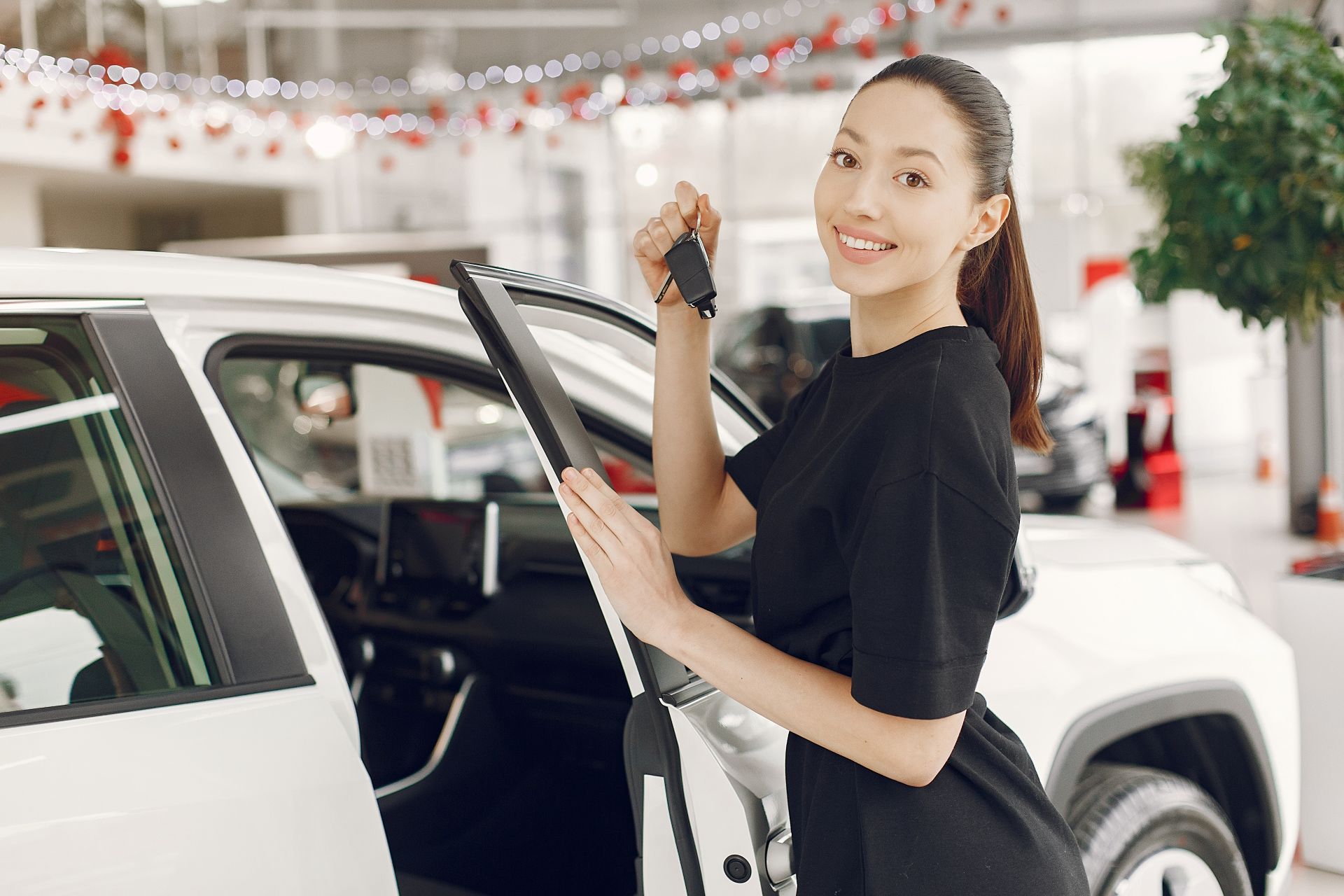 202604211491.jpg 女性在汽車展示中心打開車門並手持車鑰匙,呈現新車交車情境,象徵汽車購買與台中汽車借款免留車資金運用情境